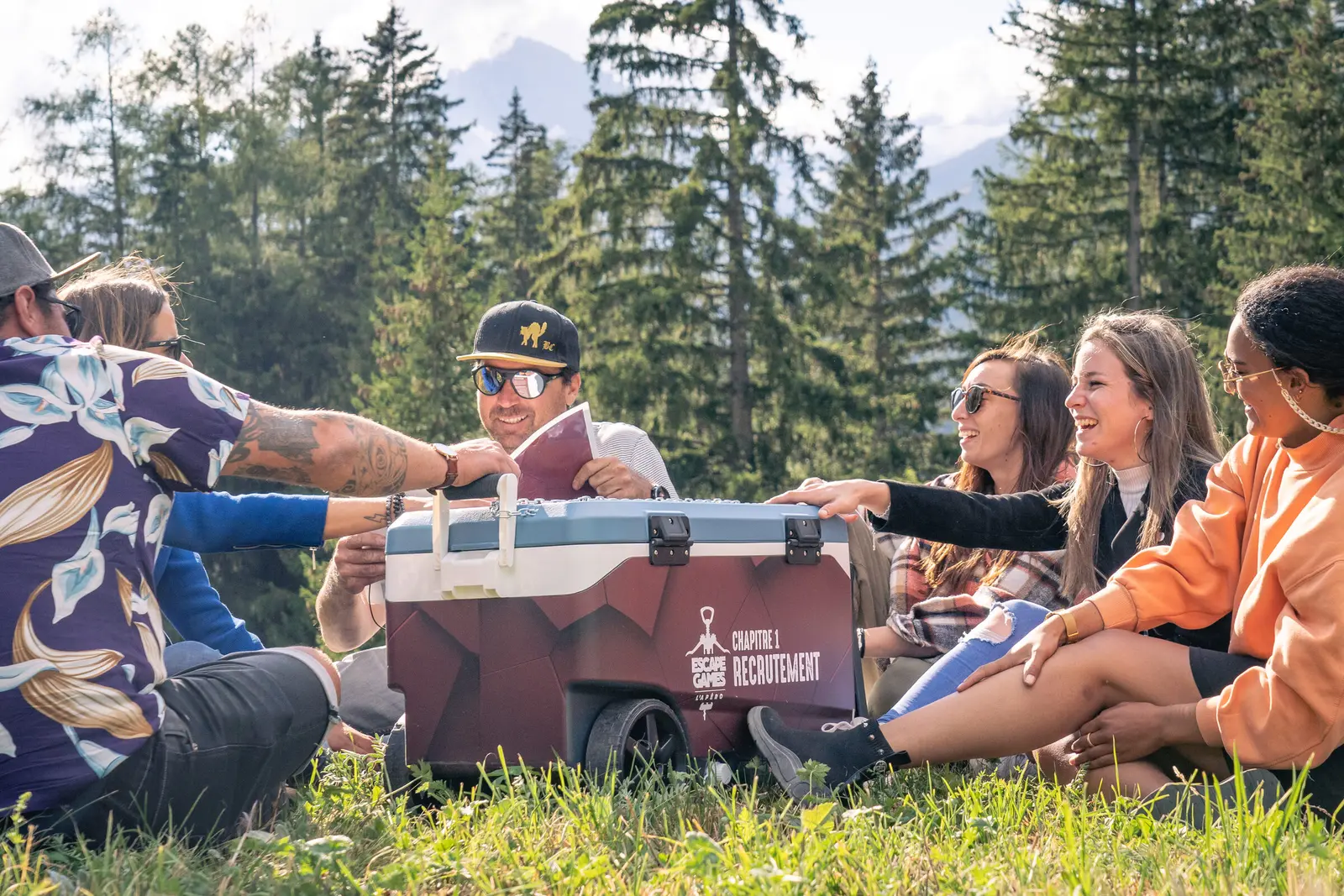 Un gruppo di amici gioca intorno alla ghiacciaia AperiEscape in un prato di montagna